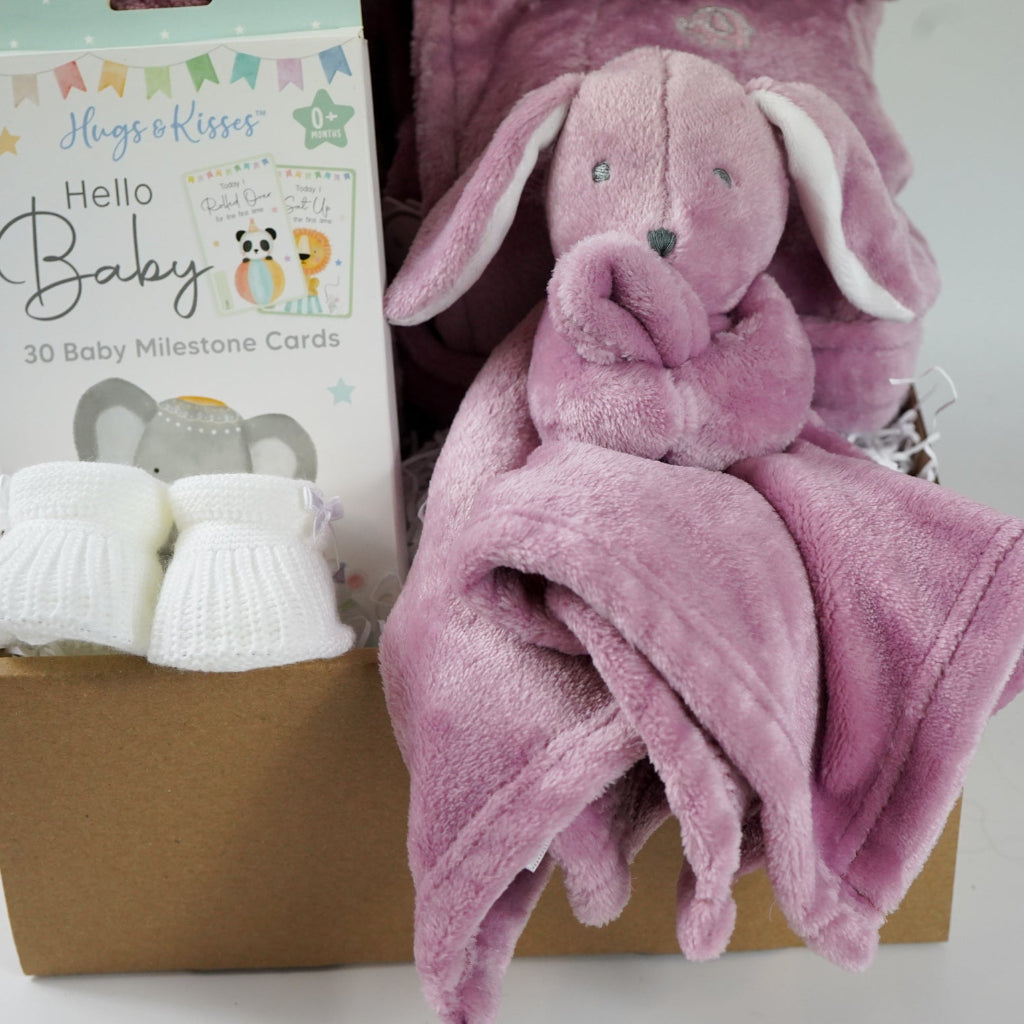 aby gift set with pink plush baby comforter in pink with matching dressing gown and blanket all in a dusky pink fleece , baby white knot hat and white knit booties and baby milestone cards packaged in a  box