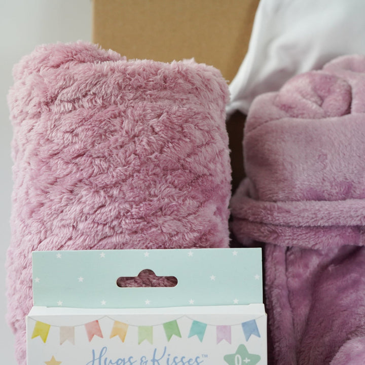 aby gift set with pink plush baby comforter in pink with matching dressing gown and blanket all in a dusky pink fleece , baby white knot hat and white knit booties and baby milestone cards packaged in a  box