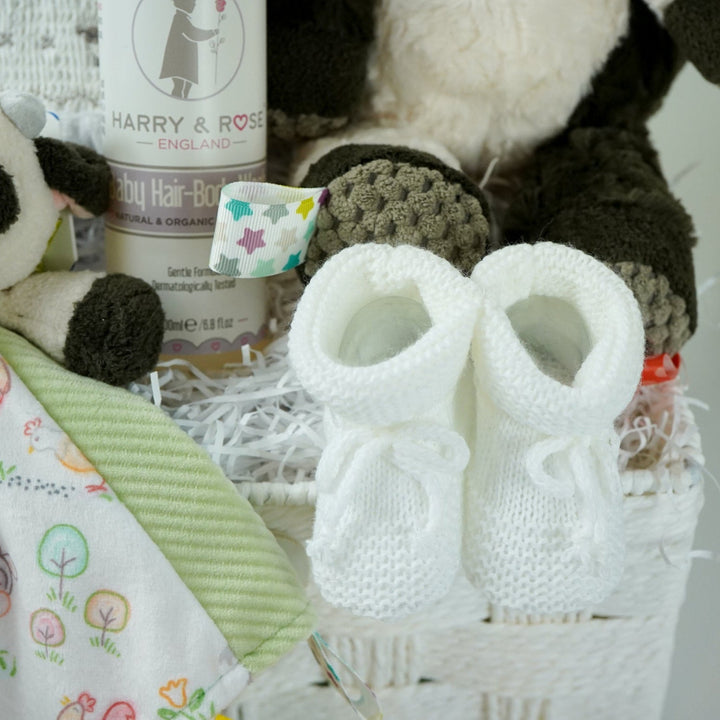 baby gift basket with a cow comforter and soft cow taggies toy, white baby sleepsuit with silver smocked sheep on bodice, organic toiletries, white knit booties and white with silver stars knot hat