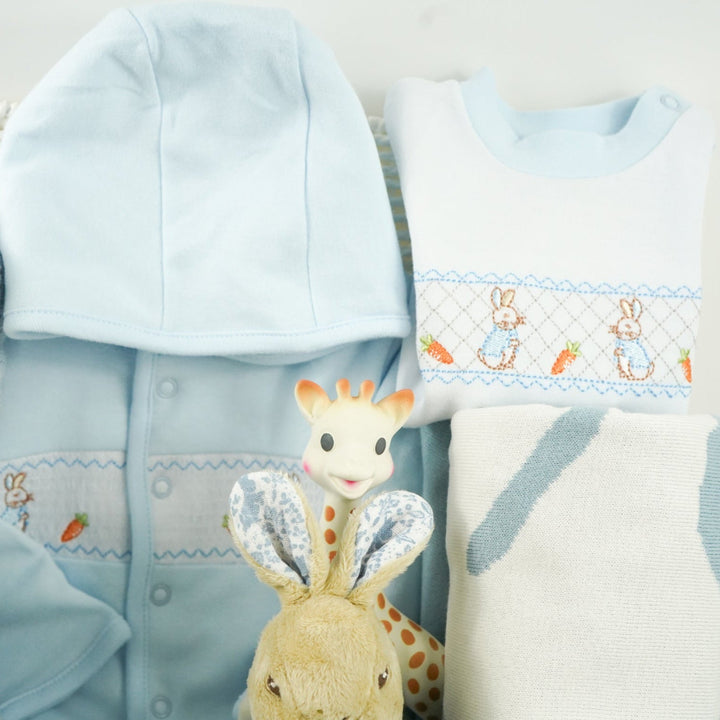 uxury baby boy gift hamper Peter rabbit themed baby clothing set includes a pale blue jacket with peter rabbit embroidered, peter rabbit comforter and soft toy, peter rabbit slippers, luxury candle, baby toiletries, cellular blanket, peter rabbit blue and white blankets with fluffy tail, Sophie La Girafee