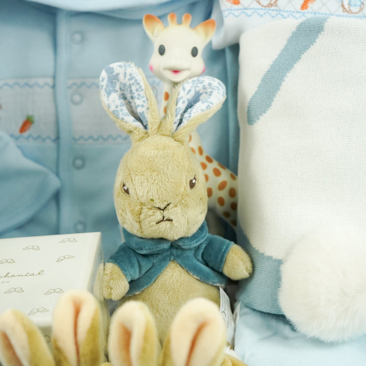 uxury baby boy gift hamper Peter rabbit themed baby clothing set includes a pale blue jacket with peter rabbit embroidered, peter rabbit comforter and soft toy, peter rabbit slippers, luxury candle, baby toiletries, cellular blanket, peter rabbit blue and white blankets with fluffy tail, Sophie La Girafee