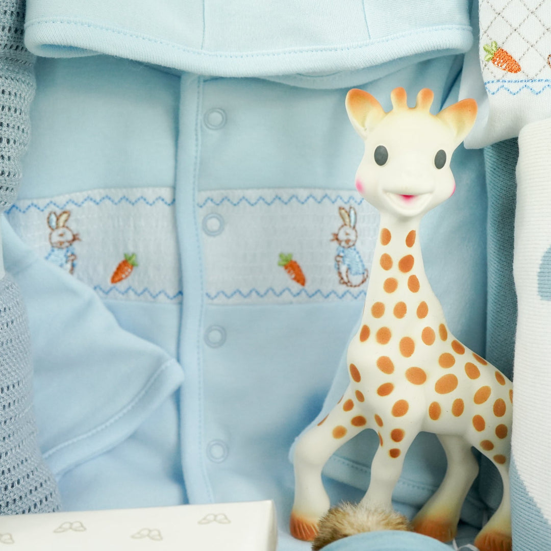 uxury baby boy gift hamper Peter rabbit themed baby clothing set includes a pale blue jacket with peter rabbit embroidered, peter rabbit comforter and soft toy, peter rabbit slippers, luxury candle, baby toiletries, cellular blanket, peter rabbit blue and white blankets with fluffy tail, Sophie La Girafee
