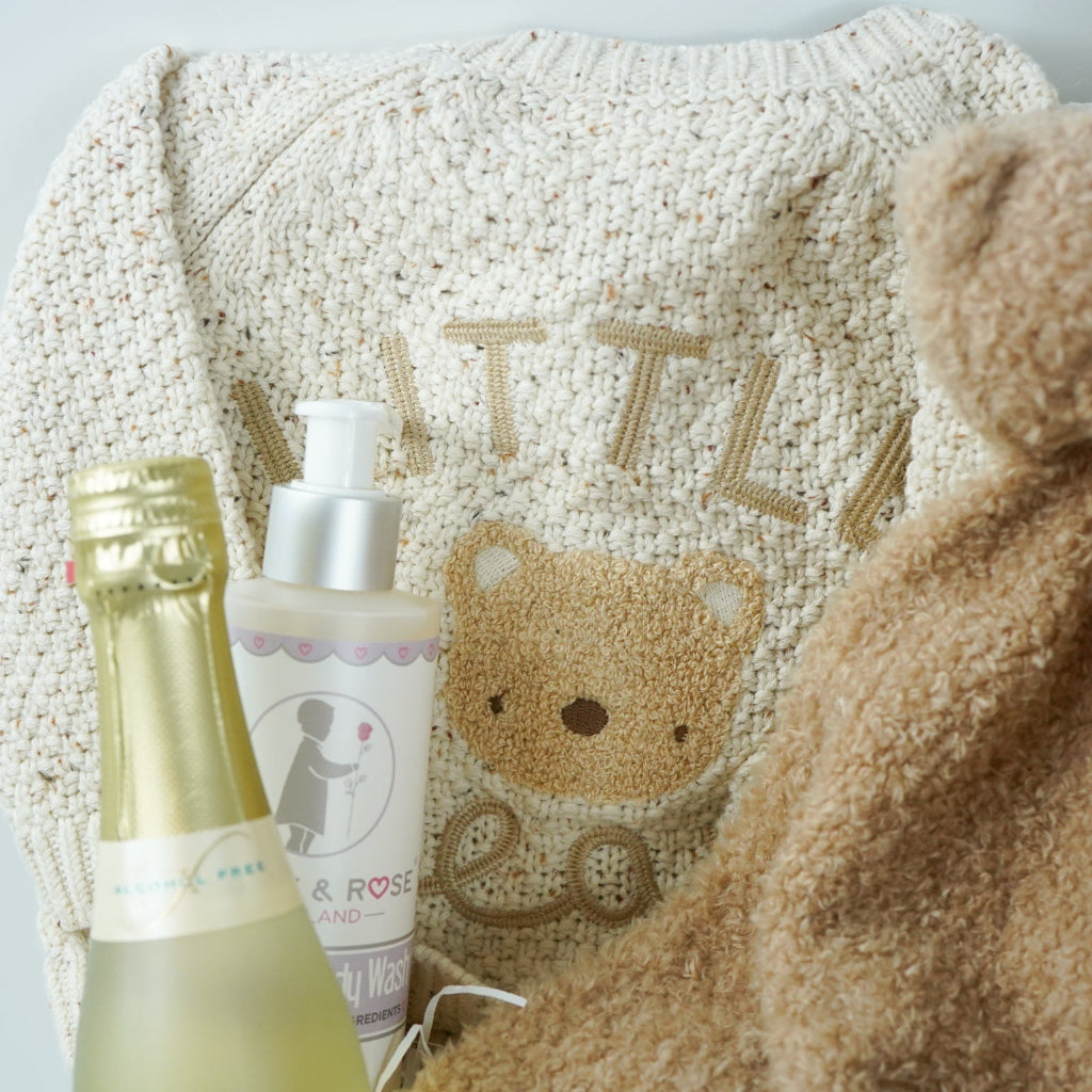 teddy themed baby gift hamper, neutral cream baby cardigan with embroidered teddy on the back, soft Nattou teddy with matching comforter, caramel coloured baby teddy booties, baby organic wash, no alcohol prosecco