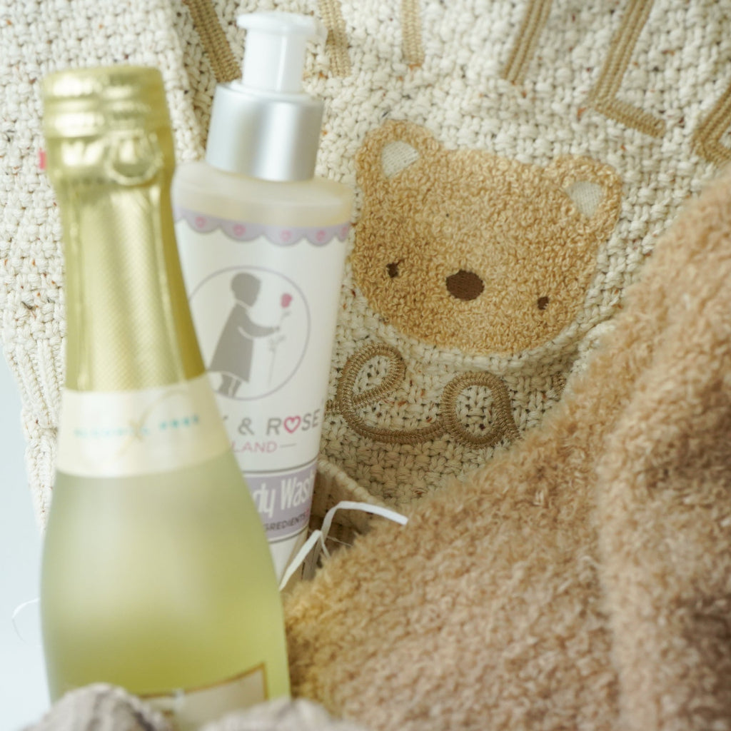 teddy themed baby gift hamper, neutral cream baby cardigan with embroidered teddy on the back, soft Nattou teddy with matching comforter, caramel coloured baby teddy booties, baby organic wash, no alcohol prosecco