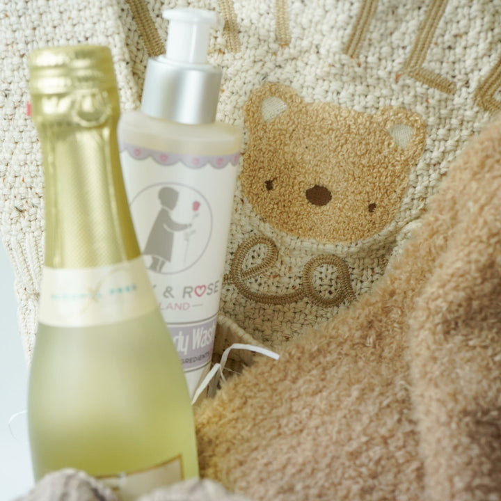 teddy themed baby gift hamper, neutral cream baby cardigan with embroidered teddy on the back, soft Nattou teddy with matching comforter, caramel coloured baby teddy booties, baby organic wash, no alcohol prosecco
