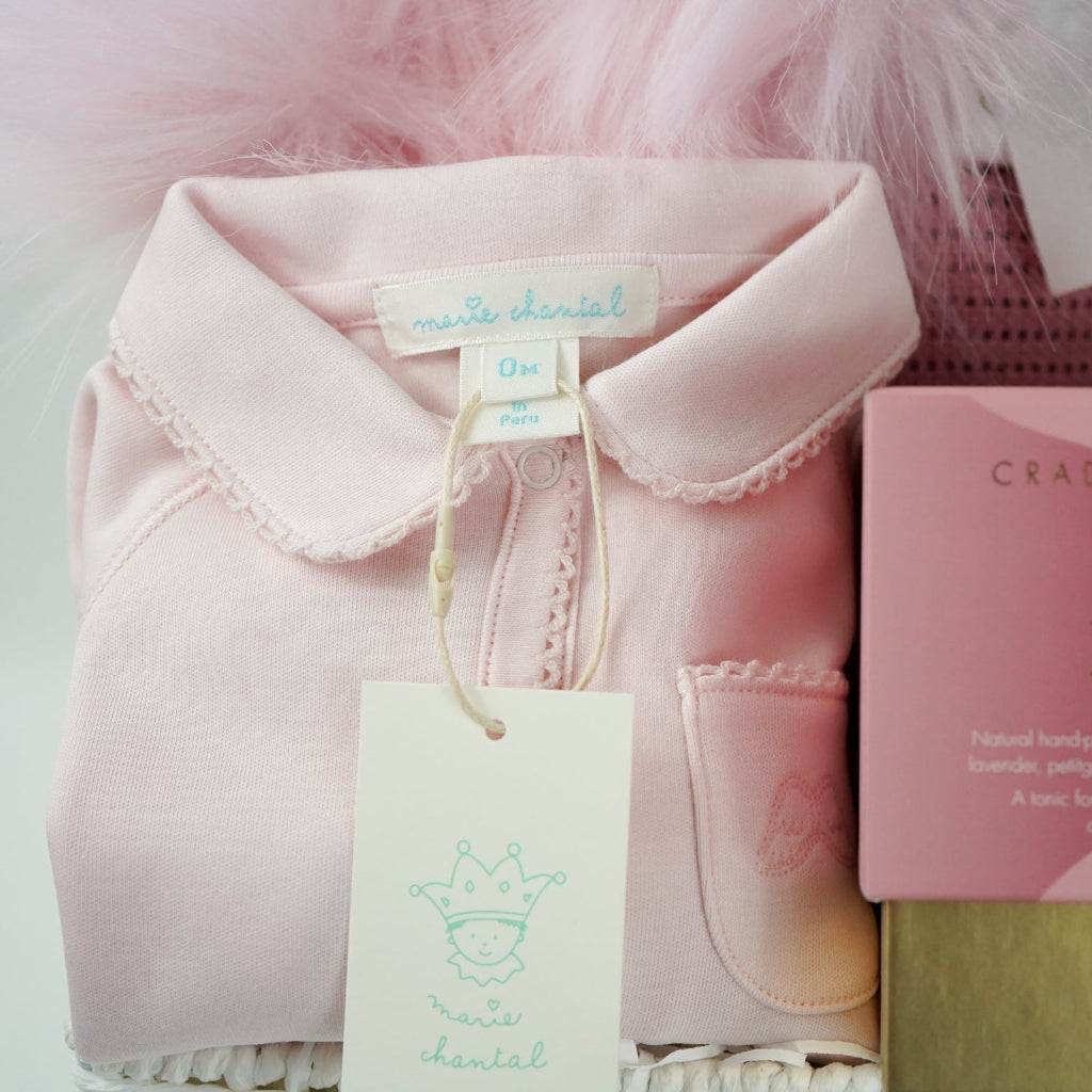 baby and mum to be hamper with luxury pink baby grow, white swaddle with butterflies, pink fluffy double pom pom hat, luxury bump candle, deep pink bamboo cellular blanket, Cuddle & Kin Artisan knitted teddy with own house, pink baby booties with a bow