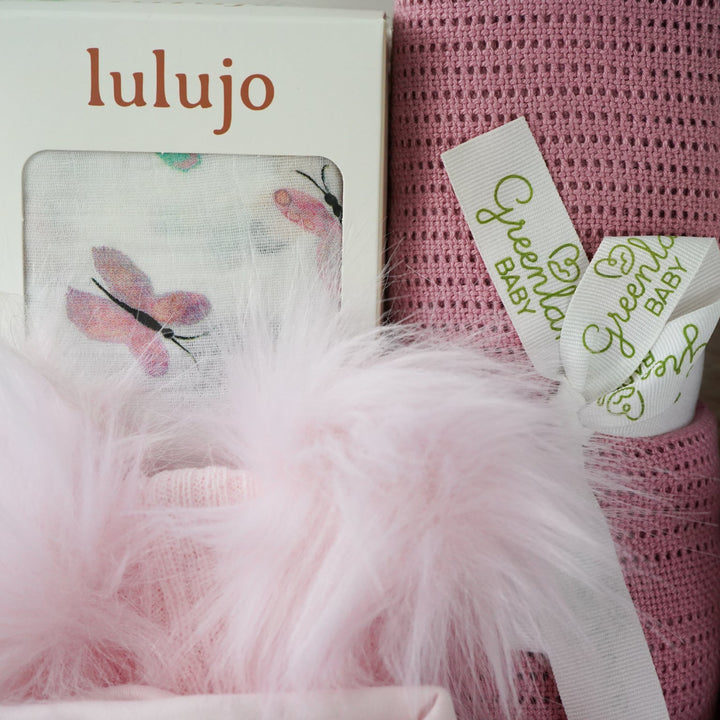 baby and mum to be hamper with luxury pink baby grow, white swaddle with butterflies, pink fluffy double pom pom hat, luxury bump candle, deep pink bamboo cellular blanket, Cuddle & Kin Artisan knitted teddy with own house, pink baby booties with a bow