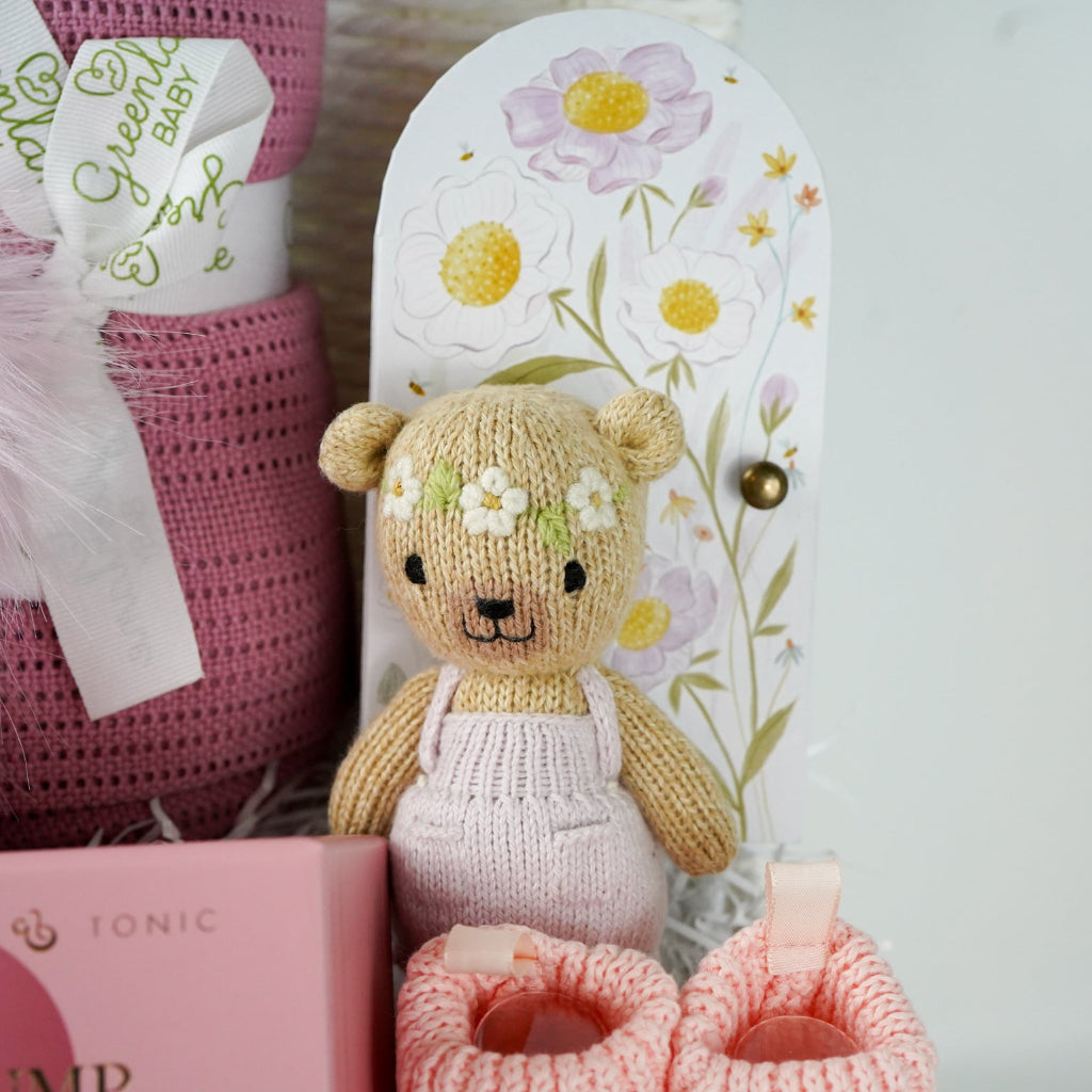 baby and mum to be hamper with luxury pink baby grow, white swaddle with butterflies, pink fluffy double pom pom hat, luxury bump candle, deep pink bamboo cellular blanket, Cuddle & Kin Artisan knitted teddy with own house, pink baby booties with a bow