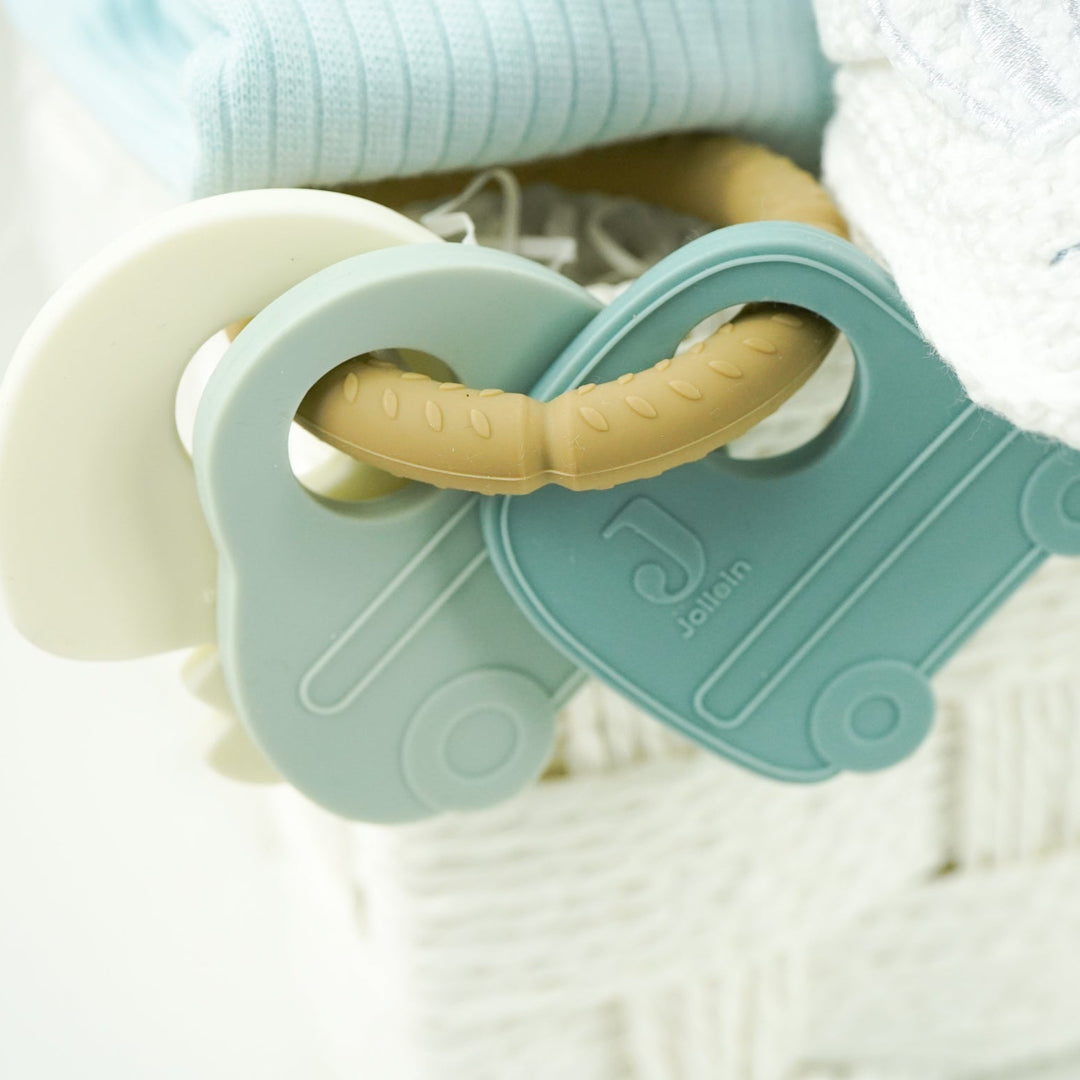 baby hamper with blue zip up baby sleepsuit, baby muslin basket in white with grey elephants, toiletries for baby, three muslins in cream with cards , car soft activity toy, white baby booties with rabbit face, silicon baby teether with 2 cars and keys in blues and cream