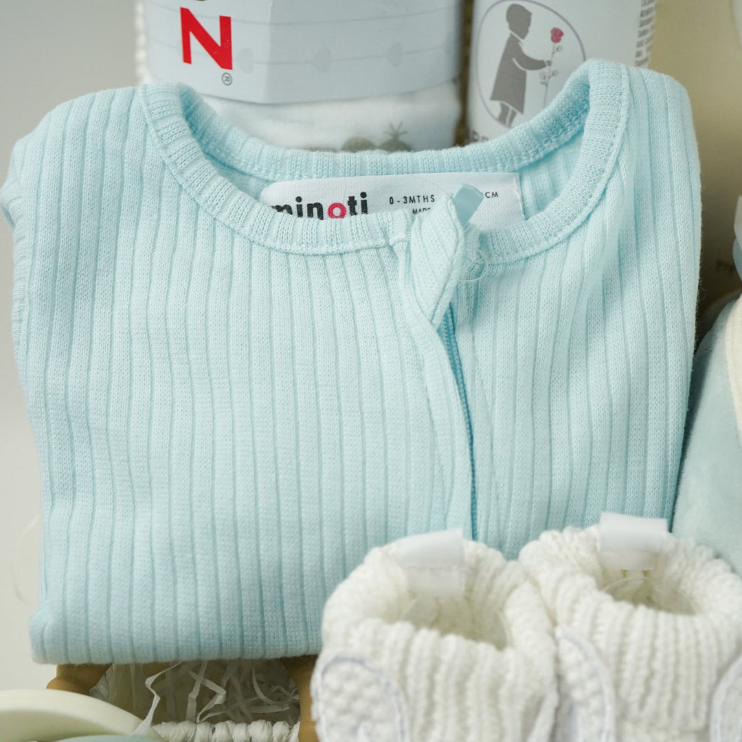 baby hamper with blue zip up baby sleepsuit, baby muslin basket in white with grey elephants, toiletries for baby, three muslins in cream with cards , car soft activity toy, white baby booties with rabbit face, silicon baby teether with 2 cars and keys in blues and cream