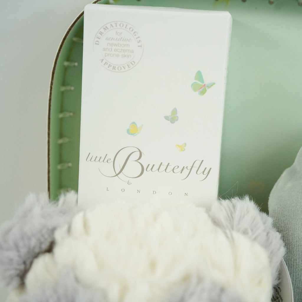 luxury neutral baby hamper in luxury baby keepsake suitcase in pale green with velour angel wings sleepsuit, organic baby toiletries, soft grey alpaca baby slippers and grey and white soft panda toy 