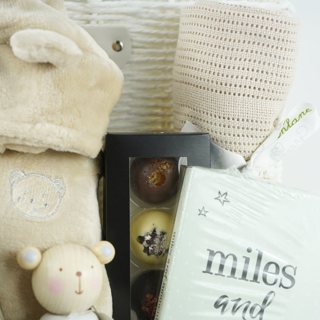 neutral baby and mum gift hamper includes neutral coloured baby dressing gown with cute ears, biscuit coloured baby pompom hat with teddy embroidery, wooden stacking toy, biscuit coloured baby booties, chocolates , milestone cards and bamboo cellular blanket 