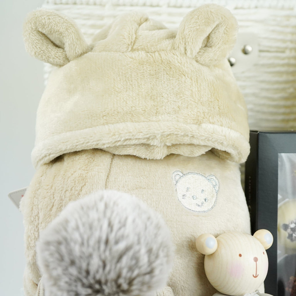 neutral baby and mum gift hamper includes neutral coloured baby dressing gown with cute ears, biscuit coloured baby pompom hat with teddy embroidery, wooden stacking toy, biscuit coloured baby booties, chocolates , milestone cards and bamboo cellular blanket 