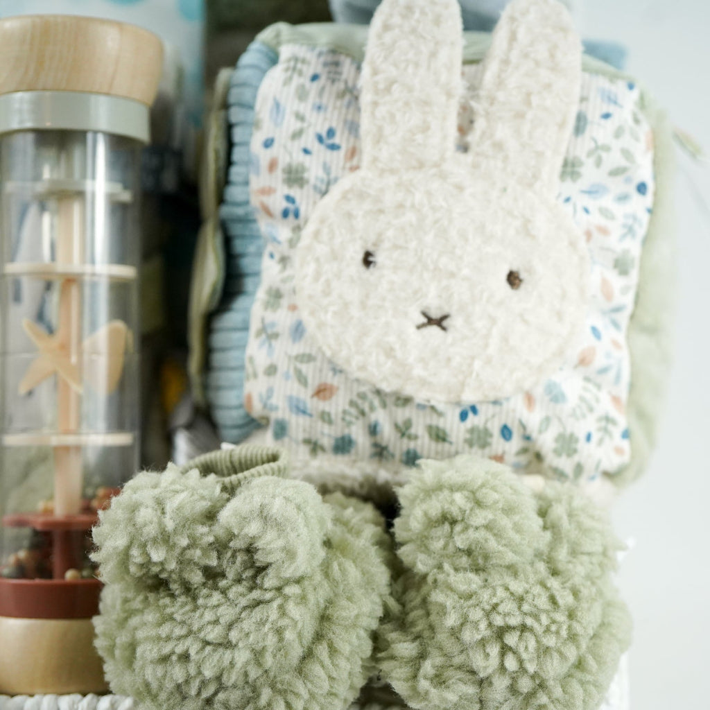 miffy themed baby hamper with green soft book, activity cube in pastel shades of green, white and blue, miffy soft rattle and matching comforter, rain rattle, blue cellular blanket, white muslin swaddle with bluebirds, fluffy green hat with ears and matching booties 