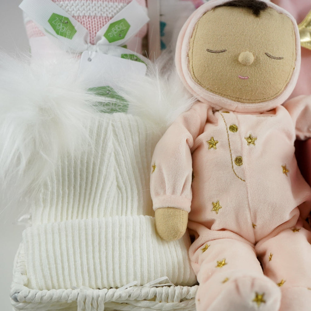 baby girl gift hamper with pink dozy dinkum soft musical doll. baby blanket , white fluffy hat, pink luxury candle, soft luxury baby outfit and swaddle in white with pink butteflies 