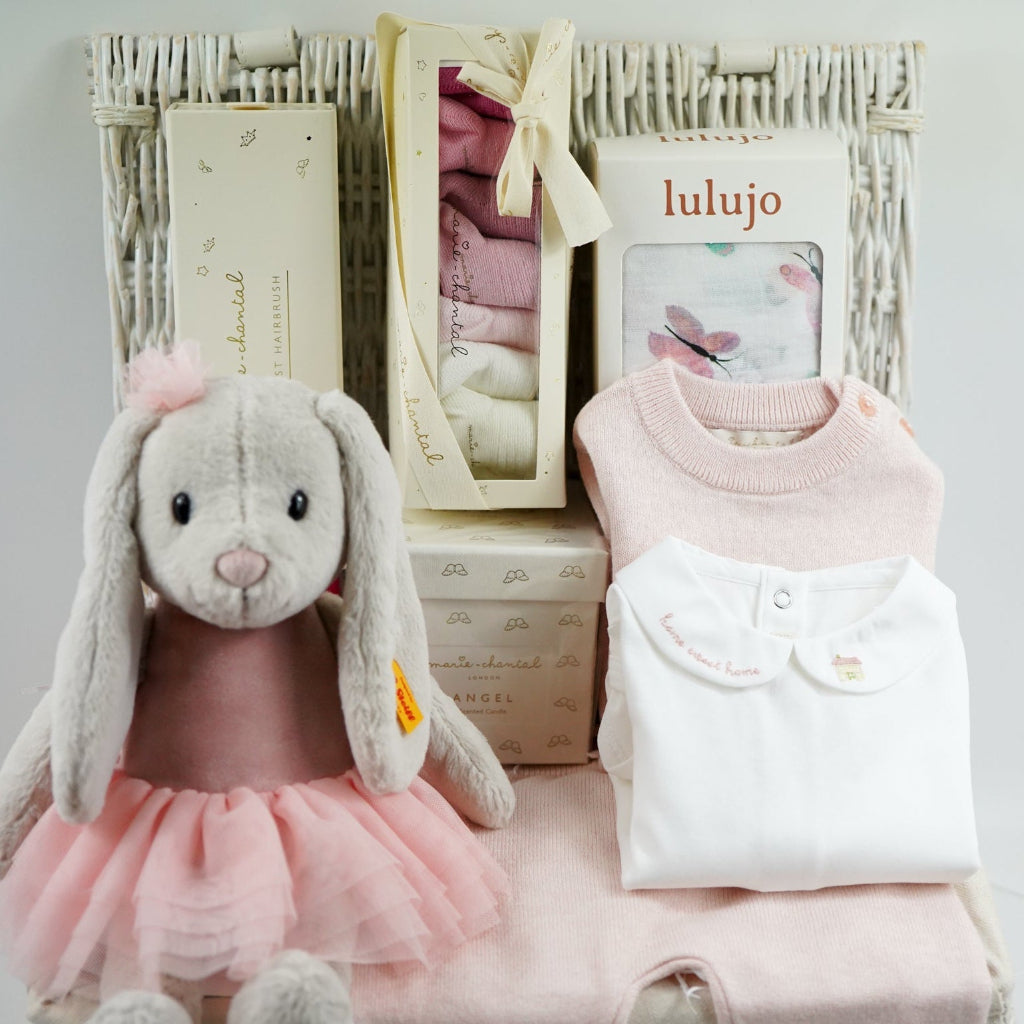 luxury baby girl gift hamper with luxury knitted baby girl outfit in pink, steiff rabbit with pink tutu, luxury hairbrush in a box, box of luxury socks, baby white swaddle with butterflies , luxury candle, white body suit with embroidered collar