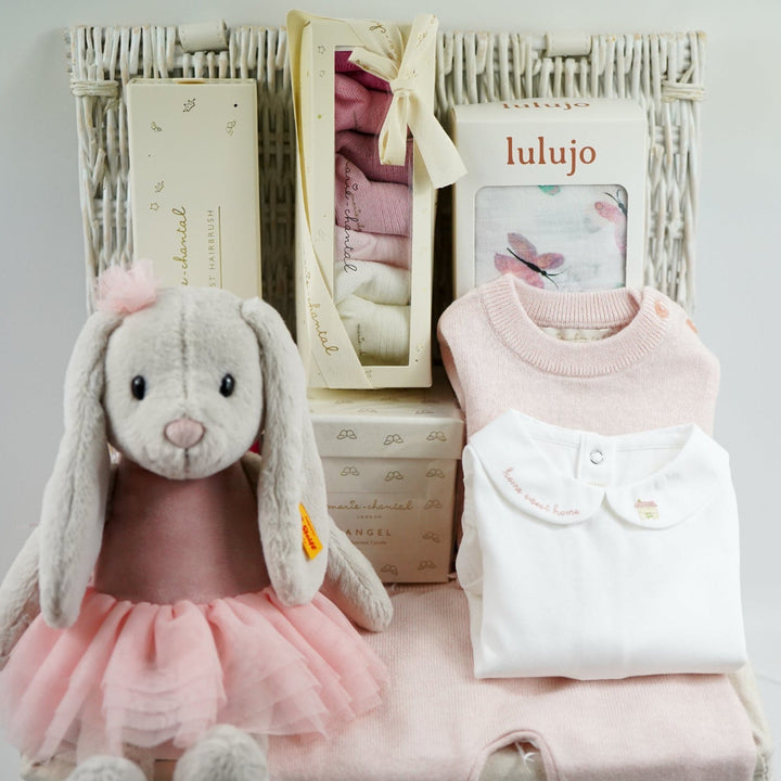 luxury baby girl gift hamper with luxury knitted baby girl outfit in pink, steiff rabbit with pink tutu, luxury hairbrush in a box, box of luxury socks, baby white swaddle with butterflies , luxury candle, white body suit with embroidered collar