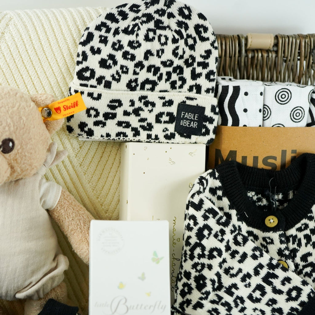 organic baby hamper with cream and black leopard prink knitted romper and  cardigan and matching hat in organic cotton, organic cotton cream blanket, organic steiff teddy, organic toiletries , organic black and white muslins and wooden sutainable hairbrush