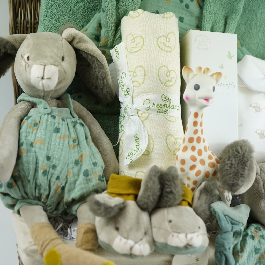 Luxury baby hamper with green hooded baby towel with ears, soft grey rabbit in green clothing set, rabbit slippers, cream and green baby swaddle, baby toiletries, green rabbit comforter, sophie la girafe teether toy, white baby sleepsuit with grey mice and magnetic fastenings all in a natural hamper basket 