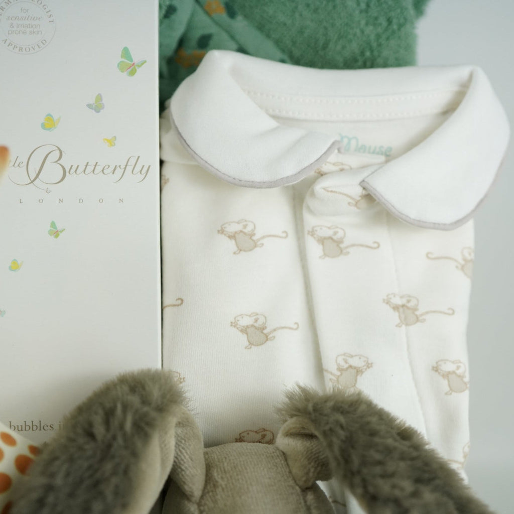 Luxury baby hamper with green hooded baby towel with ears, soft grey rabbit in green clothing set, rabbit slippers, cream and green baby swaddle, baby toiletries, green rabbit comforter, sophie la girafe teether toy, white baby sleepsuit with grey mice and magnetic fastenings all in a natural hamper basket 