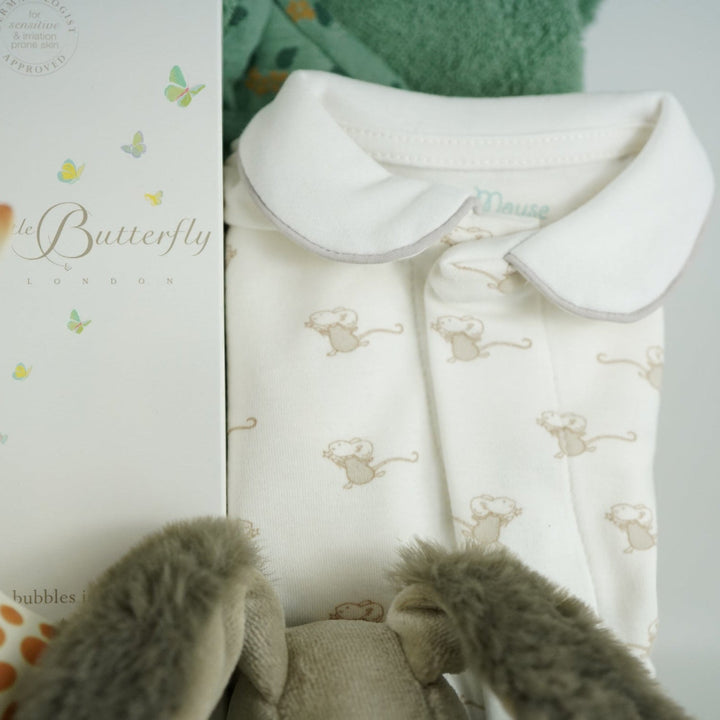 Luxury baby hamper with green hooded baby towel with ears, soft grey rabbit in green clothing set, rabbit slippers, cream and green baby swaddle, baby toiletries, green rabbit comforter, sophie la girafe teether toy, white baby sleepsuit with grey mice and magnetic fastenings all in a natural hamper basket 