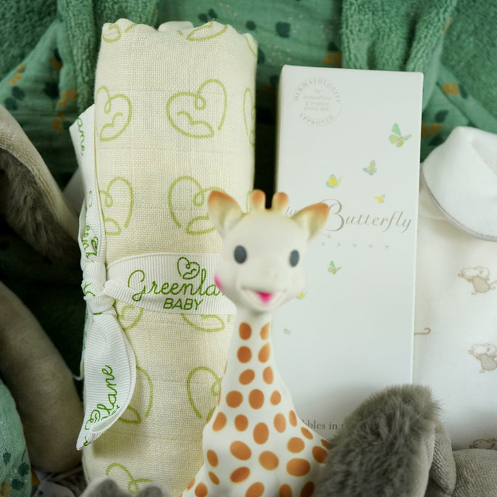 Luxury baby hamper with green hooded baby towel with ears, soft grey rabbit in green clothing set, rabbit slippers, cream and green baby swaddle, baby toiletries, green rabbit comforter, sophie la girafe teether toy, white baby sleepsuit with grey mice and magnetic fastenings all in a natural hamper basket 