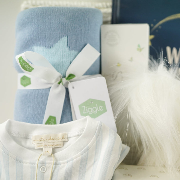 Baby clothing and items with a blue blanket, white shirt, and decorative elements on a neutral background.