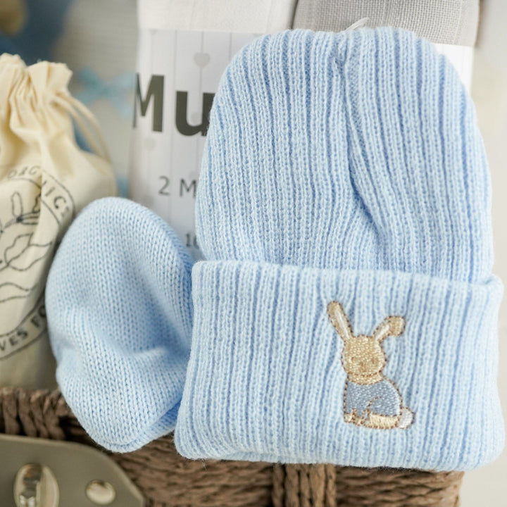 Light blue baby hat with bunny design in a basket with other baby items.