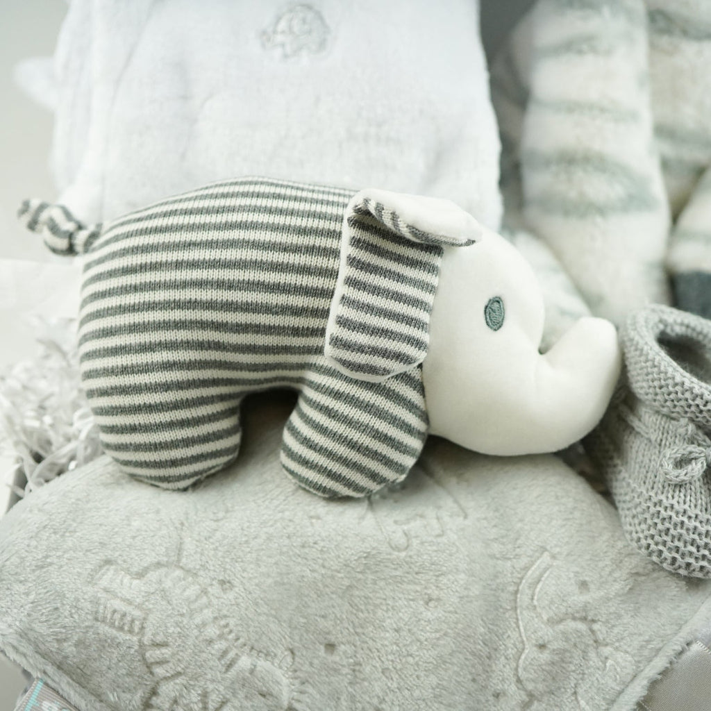 neutral baby hamper gift with a white dressing gown, soft snuggly zebra in grey and white stripes, baby rattle elephant in grey and white , soft taggie comforter, grey booties 
