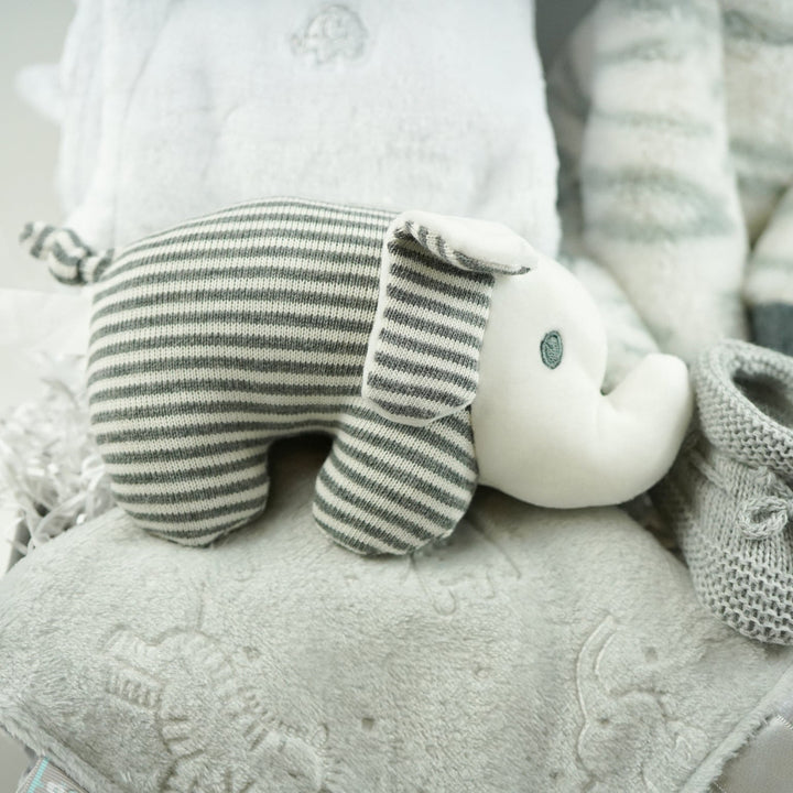 neutral baby hamper gift with a white dressing gown, soft snuggly zebra in grey and white stripes, baby rattle elephant in grey and white , soft taggie comforter, grey booties 
