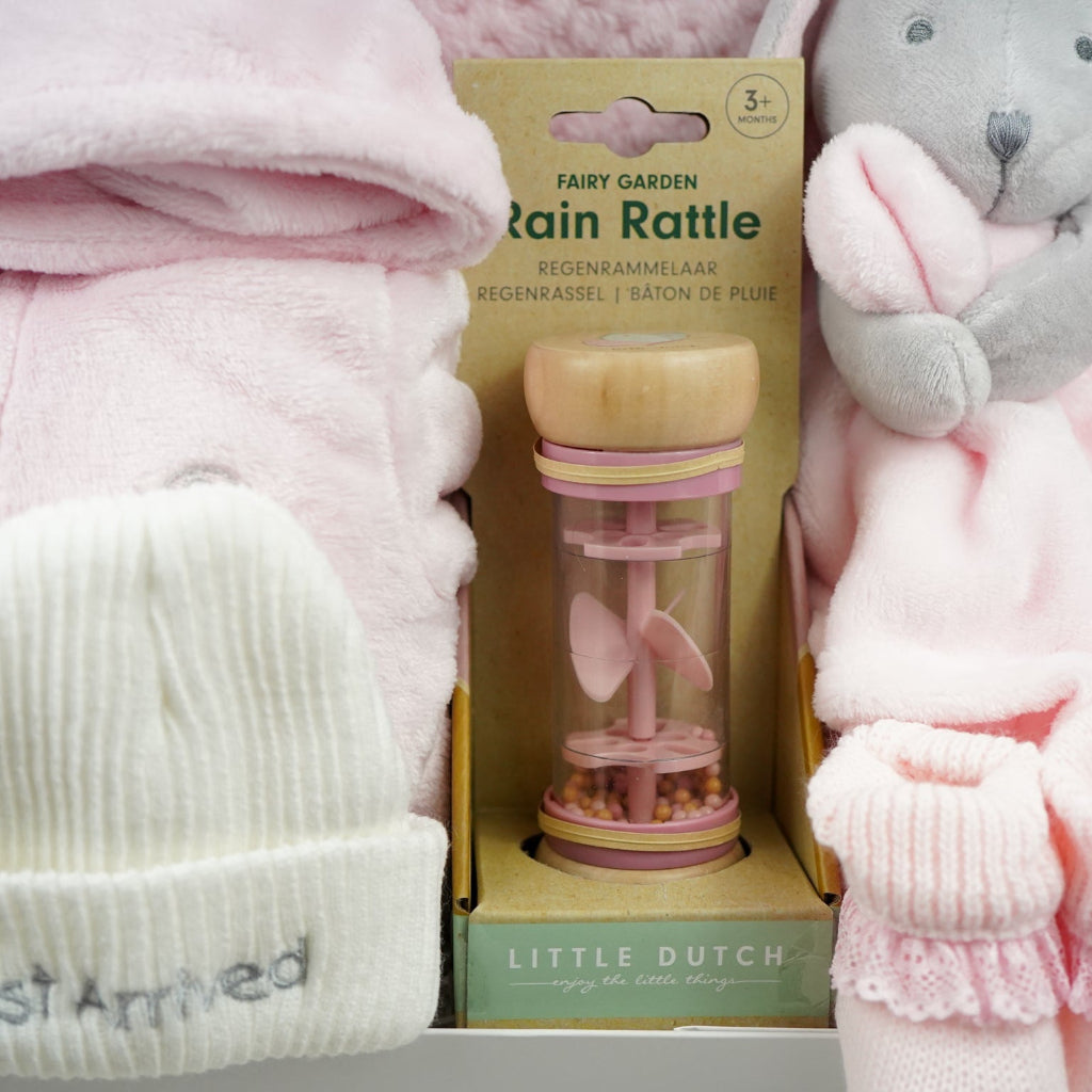 Baby items including a pink hat, rain rattle, and soft toy on a white background