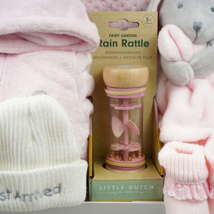 Baby items including a pink hat, rain rattle, and soft toy on a white background