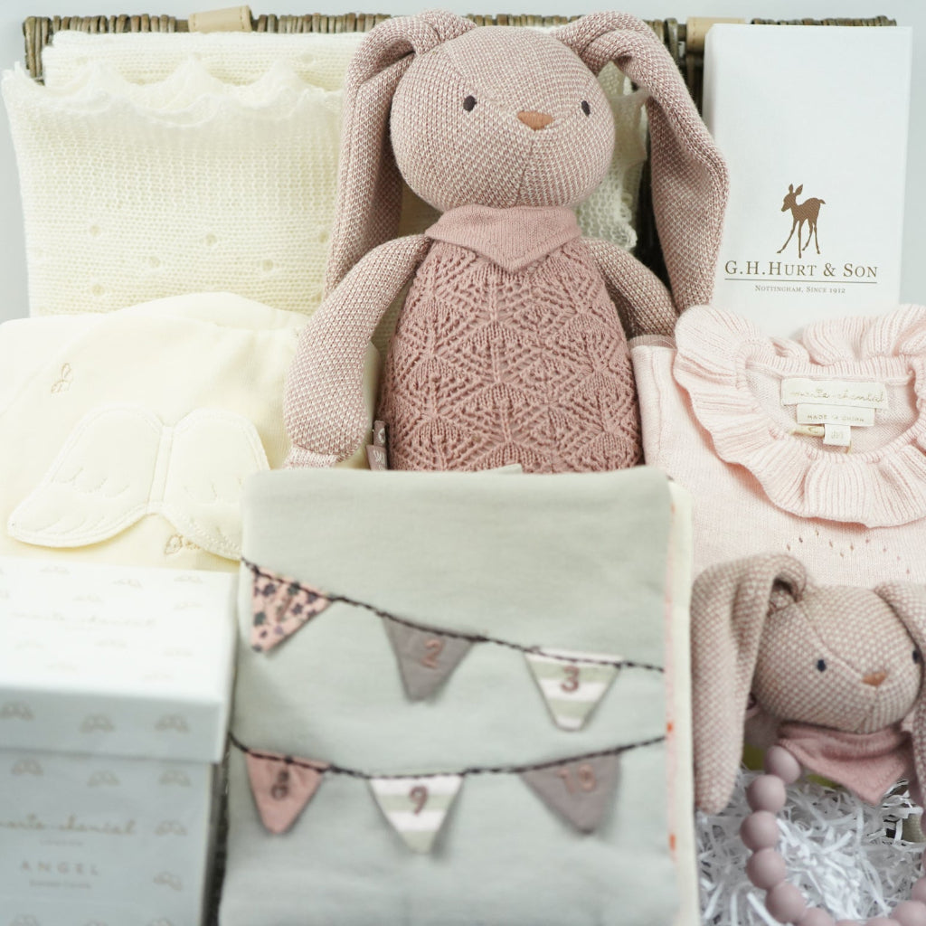 Baby gift set with pink knitted toy, headband, and blanket on a white background