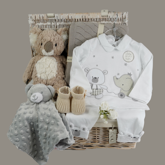 Hamper basket with baby items, soft tan koala, grey bubble teddy baby comforter, caramel coloured baby knit shoes, soft brown knit baby blanket, white baby set includes baby top with teddy and elephant, cute baby bottoms in white with teddy face and ears on the ankle cuff and teddy on the bum