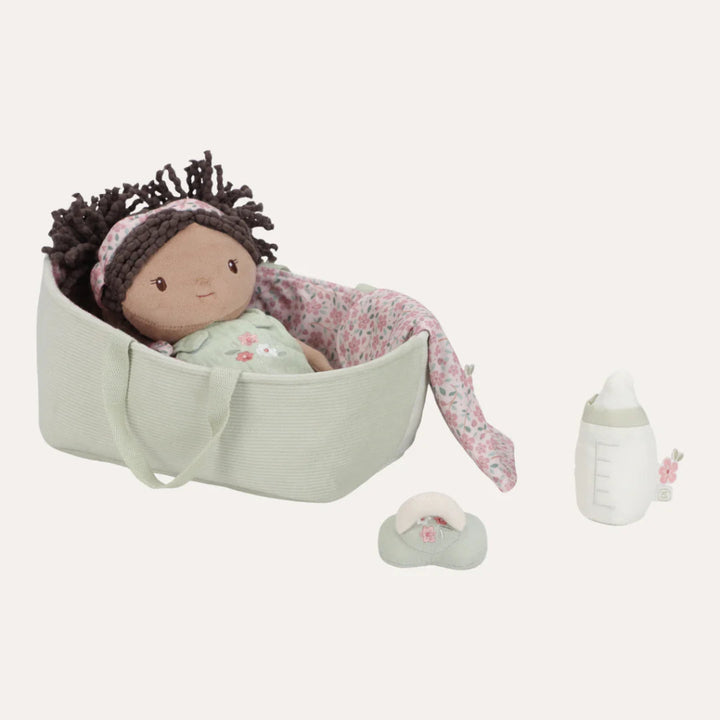 soft baby doll in a green fabric basket with a dummy, bottle and sleeping bag 