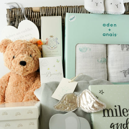 Wicker hamer with steiff teddy, baby hairbrush, Marie Chantal white candle with angel wings design, wooden teddy push a long, memorable moments cards, baby luggage lable in white PU leather with silver teddy design and matching passport holder , GH Hurt baby sharwl in grey and white with elephant design, Aden and anais swaddle muslins, marie chantal grey velour angels wings sleepsuit, marie chantal wooden baby hairbrush