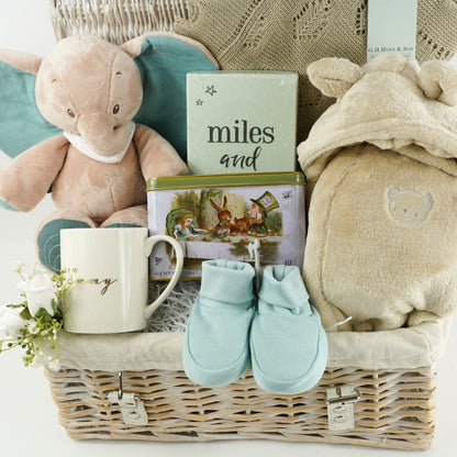 wicker hamper basket with new mum and baby gifts, new mum white mug, Alice in Wonderland tea caddy, baby memorable moments cards, Nattou soft cuddly elephant toy, G H Hurt shawl, baby dressing gown , baby organic slippers