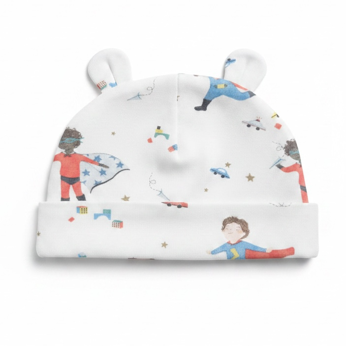 A white baby beanie hat with folded ear-like tabs on top and a folded cuff, printed with colorful cartoon superheroes and small stars.