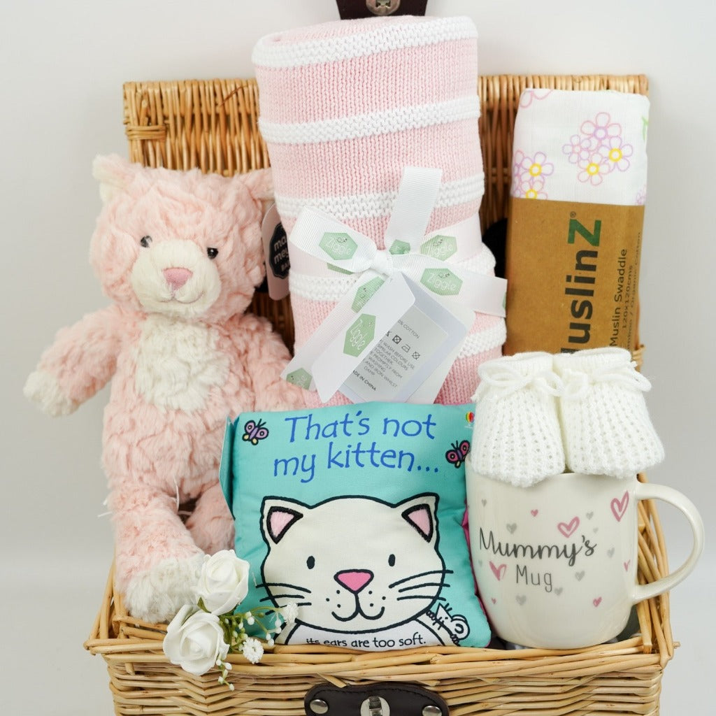 Wicker hamper with pink and white kitty soft toy, pink and white stripe heavy baby blanket, Thats Not My Kitty soft book, white baby booties, white muslin swaddle with pink flowers, mummy bone china mug