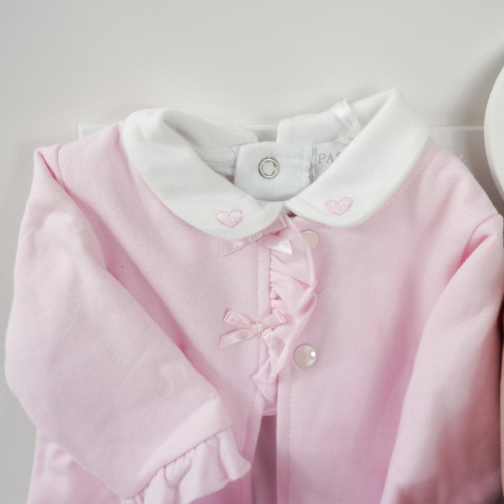 Baby hamper with pink and white baby outfit including a baby bodysuit in white with pink hearts embroidered on the collar, pink cardigan with frilled edges and bows and frilled cuffs and around the feet on the pink leggings, dusky pink star baby blanket, organic baby toiletries, white rabbit baby tuttle, pink baby shoes with a cute face and ears