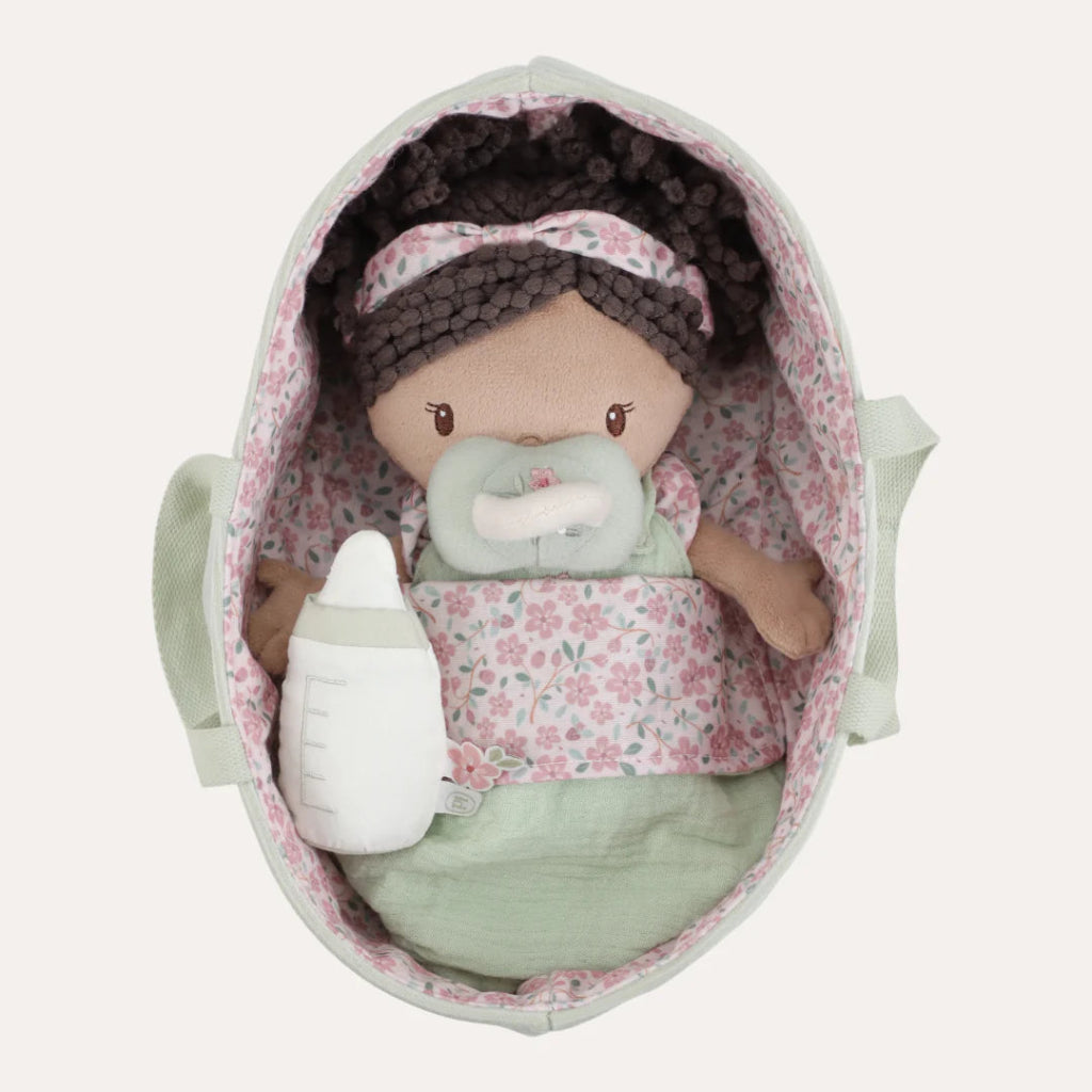 soft baby doll in a green fabric basket with a dummy, bottle and sleeping bag 