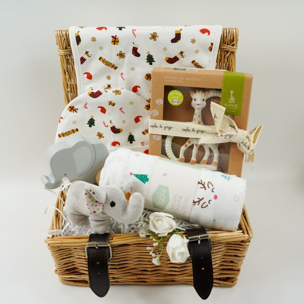 luxury cream baby christmas bib and hat set with Christmas trees, crackers, presents and stockings design, Sophie la Girafe teether, white muslin  with reindeer and christmas  trees, wooden push along elephant, Steiff crincle elephant rattle all in a small hamper basket