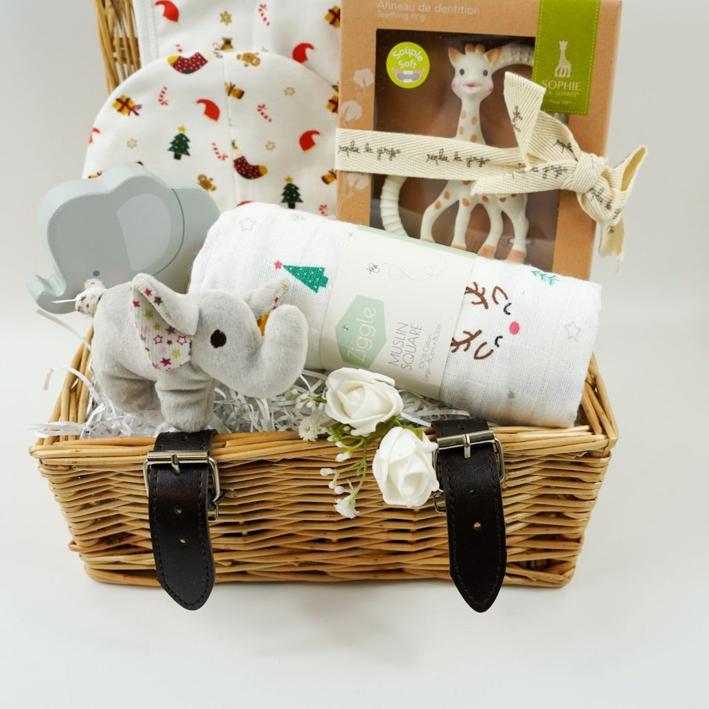 luxury cream baby christmas bib and hat set with Christmas trees, crackers, presents and stockings design, Sophie la Girafe teether, white muslin with reindeer and christmas trees, wooden push along elephant, Steiff crincle elephant rattle all in a small hamper basket