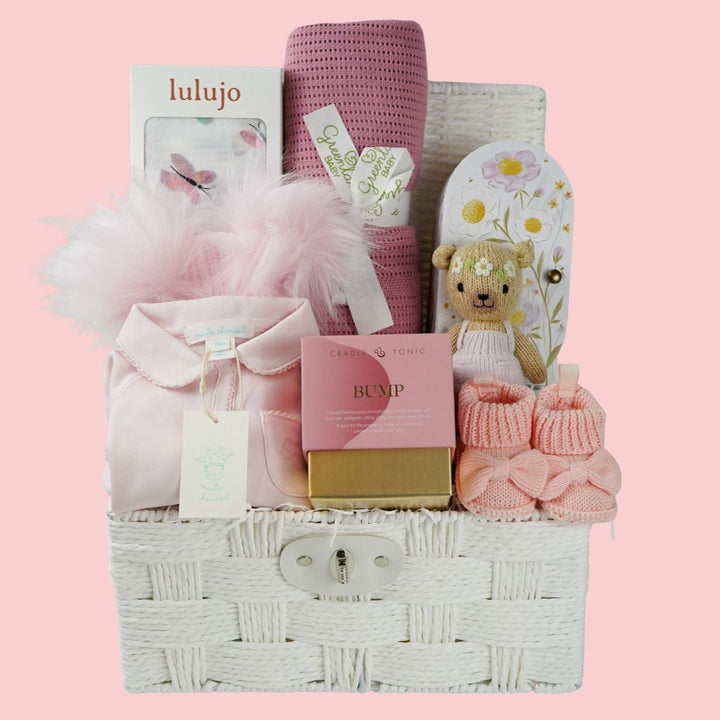 baby and mum to be hamper with luxury pink baby grow, white swaddle with butterflies, pink fluffy double pom pom hat, luxury bump candle, deep pink bamboo cellular blanket, Cuddle & Kin Artisan knitted teddy with own house, pink baby booties with a bow