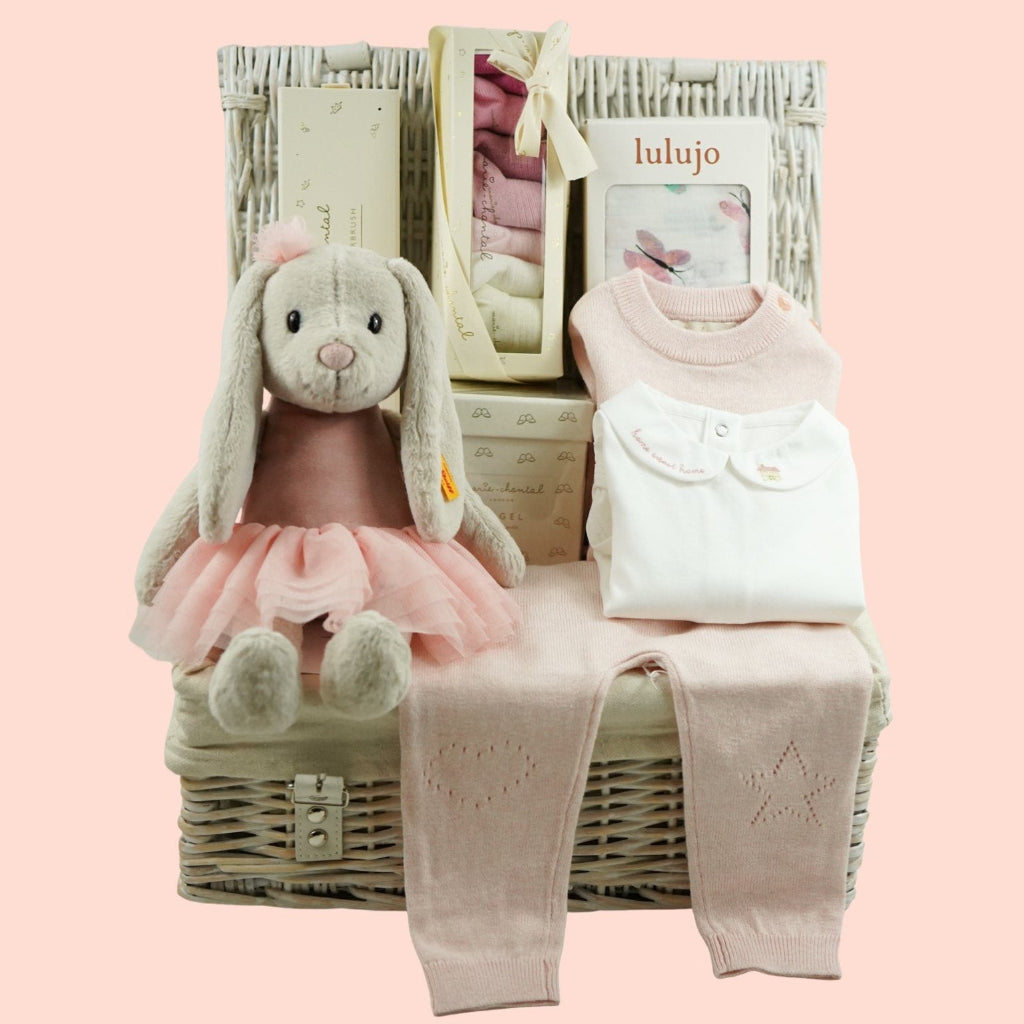 luxury baby girl gift hamper with luxury knitted baby girl outfit in pink, steiff rabbit with pink tutu, luxury hairbrush in a box, box of luxury socks, baby white swaddle with butterflies , luxury candle, white body suit with embroidered collar