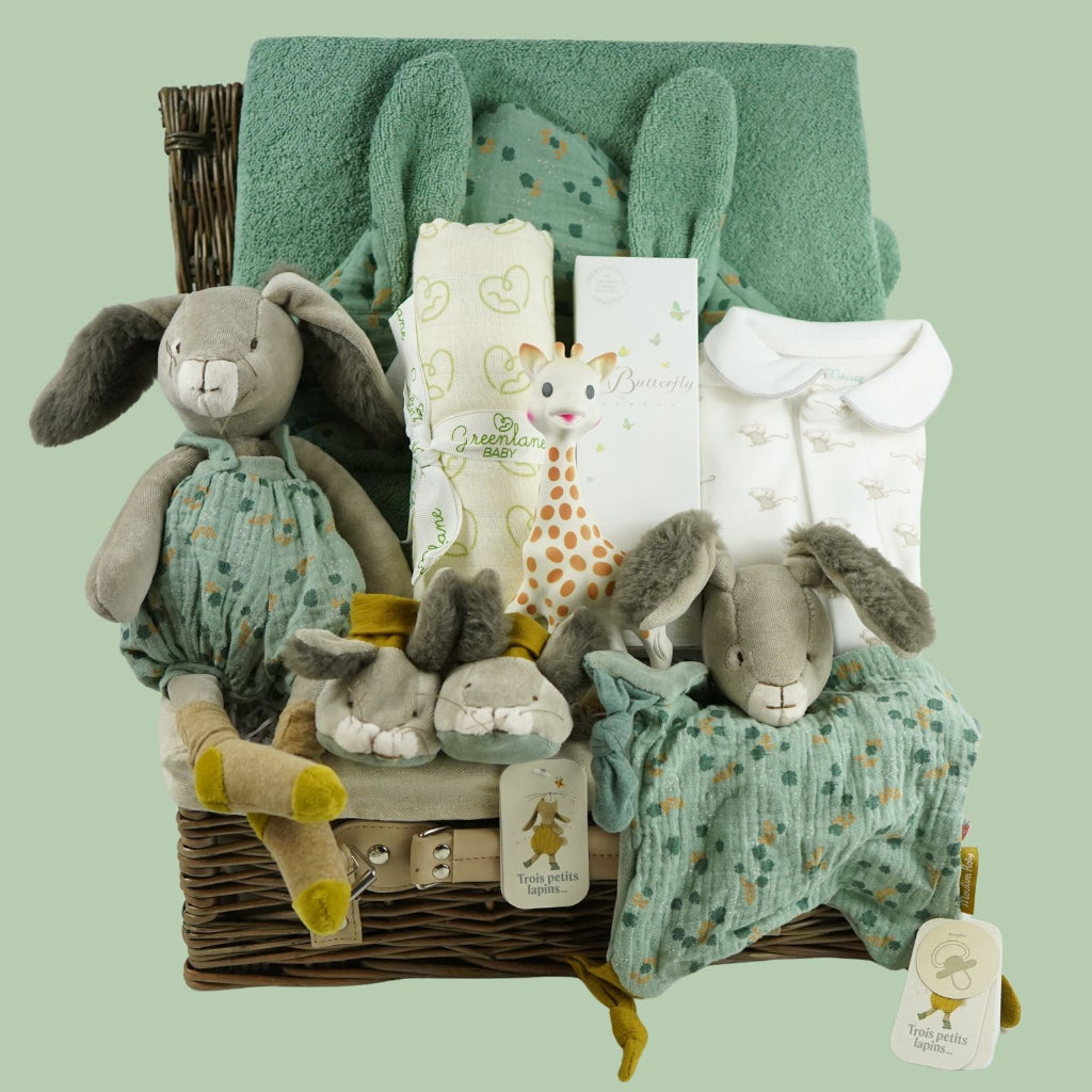 Luxury baby hamper with green hooded baby towel with ears, soft grey rabbit in green clothing set, rabbit slippers, cream and green baby swaddle, baby toiletries, green rabbit comforter, sophie la girafe teether toy, white baby sleepsuit with grey mice and magnetic fastenings all in a natural hamper basket 