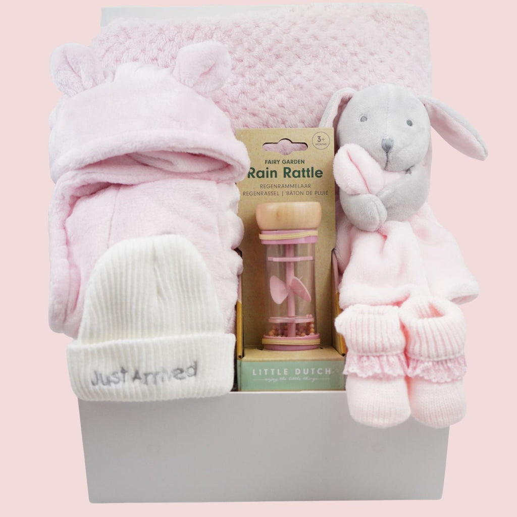 Baby gift set with pink blanket, hat, and toys on a pink background