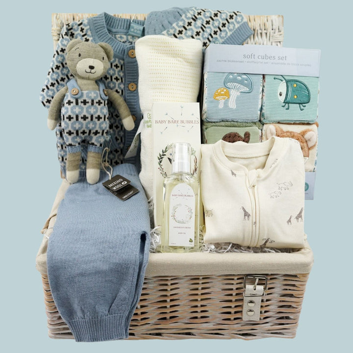 luxury baby boy gift hamper with a merino wool patterned cardigan in blue, matching leggings and hat, matching merino wool knit soft toy. Bamboo and cotton cellular blanket, baby organic toiletries, organic baby zip up cream sleepsuit with grey animals, 4 pack of baby soft cubes with woodland theme 