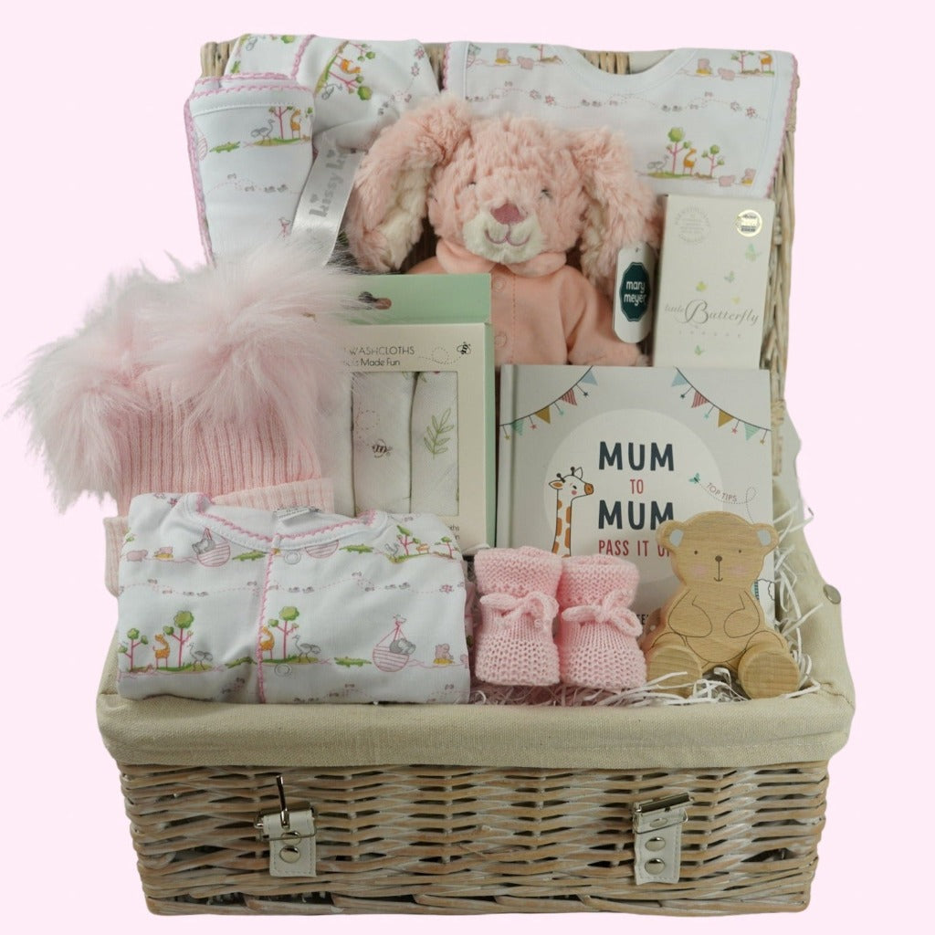 white hamper basket with Easter gifts for a baby girl, pink bunny in pink pjamas, Kissy Kissy Noahs ark baby clothing set in prima cotton includes white with pink trink sleepsuit, bib and hat, Noah's Ark pattern pink and white baby blanket, baby wash cloths with bunnies, Organic baby wash, pink knit booties, wooden teddy, pink fluffy double pom pom baby hat, mum to mum book full of tips