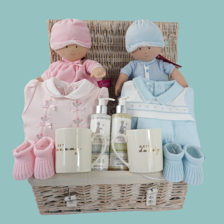 Twin baby hamper includes pink luxury baby girl outfit with a white collar and bows, blue baby boy outfit with a blue collar and white yolk, pink soft baby ragdool with a pink hat, blue soft baby ragdoll with sriped blue and white outfit and blue hat, pink booties and blue booties, organic baby lotion and organic bubble bath , new mummy and daddy cream bone china mug